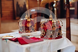 Two beautiful crowns with gold and red cloth stand on a table in the church before the baptism of the baby