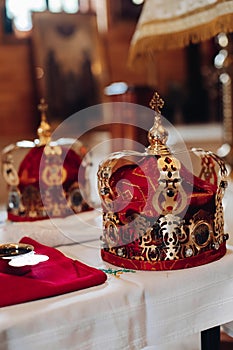 Two beautiful crowns with gold and red cloth stand on a table in the church before the baptism of the baby