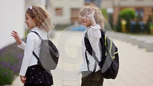 Two beautiful curly-haired children, a boy and a girl, go to school. They turn and wave their hands at parting. Goodbye