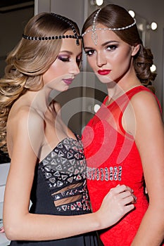 Two beautiful elegant girl in a red and black evening dresses with bright evening make-up evening hairstyle and ticks on his