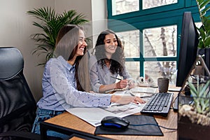 Two beautiful female designers or architects jointly solve work tasks while working in modern office near window