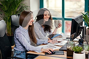 Two beautiful female designers or architects jointly solve work tasks while working in modern office near window