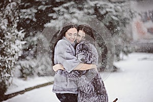 Two beautiful girlfriends hugging and smiling outdoors in winter. Two young female friends portrait closeup. Retouched, natural