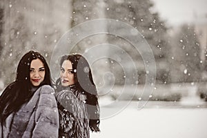 Two beautiful girlfriends hugging and smiling outdoors in winter. Two young female friends portrait closeup. Retouched, natural