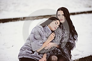 Two beautiful girlfriends hugging and smiling outdoors in winter. Two young female friends portrait closeup. Retouched, natural