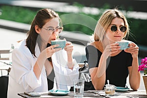 Two beautiful girls with cups coffee in summer cafe. Girl friends in cafe outdoor. Outdoors portrait of two young