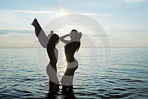Two beautiful girls are dancing on the beach at sunset sea background, silhouettes