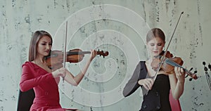 Two beautiful girls in dresses playing the violin emotional on background