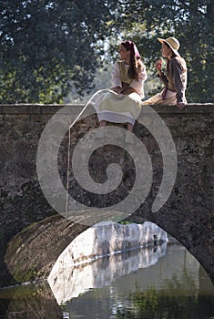 Two beautiful girls fishing from a bridge in a medieval event `Viagem Medieval em Terra de Santa Maria`, Santa Maria da Feira. photo