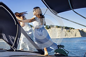 Two beautiful girls in light color summer dresses are resting on a ship