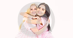 Two beautiful girls in pajama hugs. Best friends concept. Ladies on smiling faces hugs each other tight, white