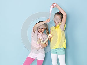 Two beautiful girls playing with homemade slime and having a lot of fun in front of blue background