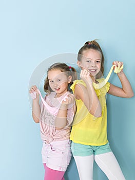 Two beautiful girls playing with homemade slime and having a lot of fun in front of blue background