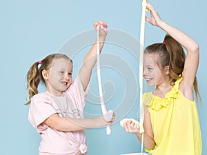 Two beautiful girls playing with homemade slime and having a lot of fun in front of blue background