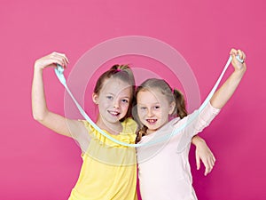 Two beautiful girls playing with homemade slime and having a lot of fun in front of pink background