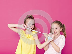 Two beautiful girls playing with homemade slime and having a lot of fun in front of pink background