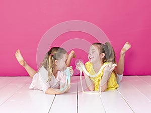 Two beautiful girls playing with homemade slime and having a lot of fun in front of pink background