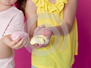 Two beautiful girls playing with homemade slime and having a lot of fun in front of pink background