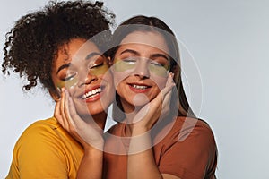 Two beautiful girls posing close to each other cheek to cheek, with applied under eye gel pads