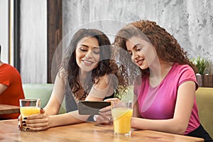 Two girls sitting in cafe, drinking juice and doing selfie