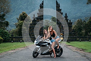 Two beautiful girls are sitting on a motorcycle colour black and white. Models dressed in black jerseys and denim