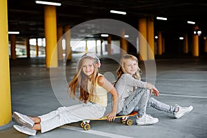 Two beautiful girls skateboarding, having fun and playing in the parking lot