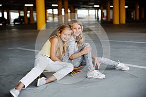 Two beautiful girls skateboarding, having fun and playing in the parking lot