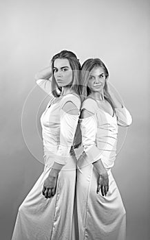 Two beautiful girls stand in a studio.They wear light silk dresses. Two is blonds.