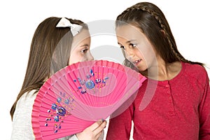 Two beautiful girls talking behind oriental fan whisper playing