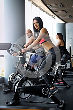 Two beautiful girls with their coach working out of cycling in modern fitness club