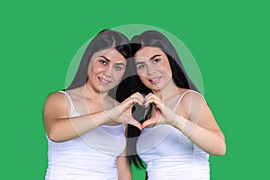 Two beautiful girls in white t-shirt with straps leaned against each other and put their hands together and made heart