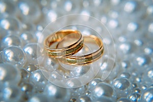 Two beautiful gold wedding rings lie among the white pearls, selective focus, close-up. Wedding concept