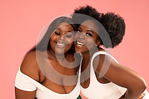 Two beautiful happy women with amazing toothy smiles posing together on pink pastel studio background. Friendship and happiness
