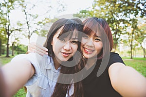 Two beautiful happy young asian women friends having fun together at park and taking a selfie.