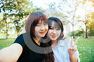 Two beautiful happy young asian women friends having fun together at park and taking a selfie.