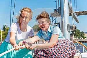 Two beautiful and joyful girls pull a rope on a yacht on the deck, laugh and joke.