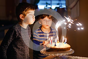 Two beautiful kids, little preschool boys celebrating birthday and blowing candles on homemade baked cake, indoor