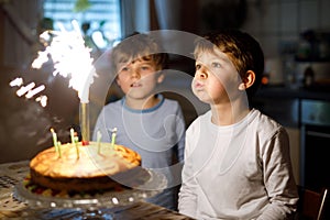 Two beautiful kids, little preschool boys celebrating birthday and blowing candles on homemade baked cake, indoor