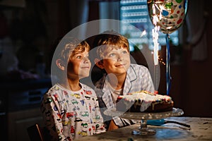 Two beautiful kids, little preschool boys celebrating birthday and blowing candles on homemade baked cake, indoor