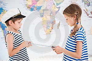 Two beautiful kids in sailor striped shirts measure distance on world map with measuring tape