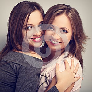 Two beautiful laughing girl friends looking with love and natural tenderness emotion on blue background. Toned closeup portrait