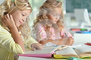 Two beautiful little girls at class read book and writing at not