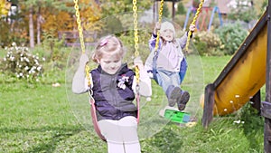 Two beautiful little girls on a swings outdoor in the playground