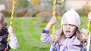 Two beautiful little girls on a swings outdoor in the playground