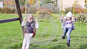 Two beautiful little girls on a swings outdoor in the playground