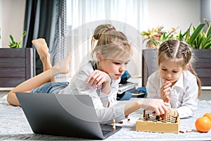 Two beautiful little sisters playing chess on a floor in living room