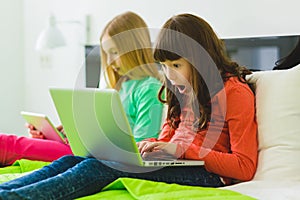 Two beautiful little sisters sitting on bed and play with a Tablet or laptop