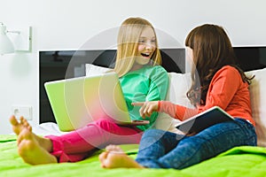 Two beautiful little sisters sitting on bed and play with a Tablet or laptop