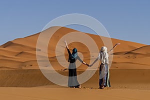 Two Beautiful Models Pose In The Sand Dunes In The Great Sahara Desert In Morocco, Africa