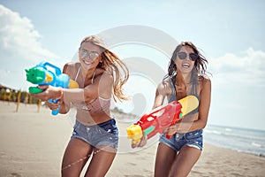 Two sexy young female with sunglasses playing with water-gun on sandy beach